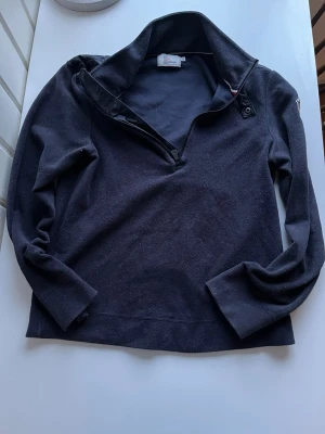 Mörkblå fleece tröja från Moncler - Säljer en mörkblå fleece tröja från Moncler Grenoble med halv dragkedja och hög krage. Tröjan har broderad logga på ärmen och är långärmad. Perfekt för kyliga dagar och riktigt skön att ha på sig.