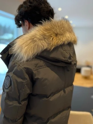 Grå dunjacka Canada Goose med päls - Säljer en grå dunjacka från Canada Goose med avtagbar pälskrage. Jackan har en klassisk pufferstil, huva och tydlig logga på ärmen. Perfekt för kalla dagar och riktigt snygg till vinterlooken.