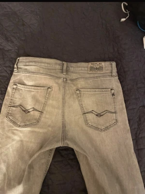 Grå Replay jeans straight fit - Snygga grå jeans från Replay med klassisk femficksdesign och raka ben. Jeansen har svarta detaljer på bakfickorna och Replay-logga på myntfickan. Perfekta för dig som gillar en stilren och enkel look.