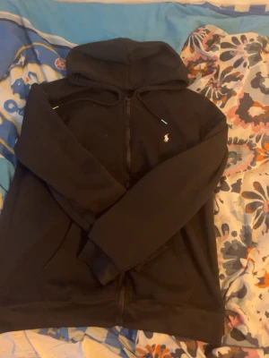 Svart Polo Ralph Lauren zip up hoodie - Snygg och stilren svart zip-up hoodie från Polo Ralph Lauren. Storlek M, men passar S perfekt för en lite mer tajt och clean passform. Väldigt skön, bra kvalitet och sitter riktigt bra på kroppen. Passar alla årstider och är lätt att matcha – funkar till allt från jeans till mjukis. Nyskick, endast använd en gång. Hör av dig vid frågor, kan sänka priset också 💯
