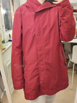 Röd regnjacka från Everest strl 40 - Säljer en röd regnjacka från Everest i storlek 40. Jackan har huva, dragkedja och fickor med dragkedja. Materialet är vattentätt och jackan har en clean, enkel design som passar perfekt när det regnar. TCS Waterproof med tejpade sömmar.