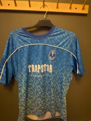 Blå mönstrad Trapstar topp S - Säljer en blå kortärmad topp från Trapstar med vit text och nummer 22 på ryggen. Den är är overzized. Hör av dig om du är intresserad!