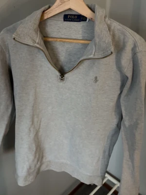 Grå half zip tröja Polo Ralph Lauren - Säljer en stilren grå tröja från Polo Ralph Lauren med half zip och klassisk krage. Tröjan har lång ärm och diskret broderad logga på bröstet. Perfekt till chill vardagsstil och enkel att matcha med jeans eller sweatpants.