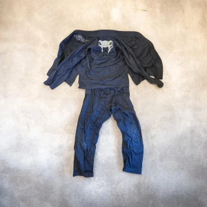 Blå Venum träningsväst - Säljer en grå bjj set från Venum med broderad logga på bröstet och coolt tryck på ryggen. Västen är gjord i slitstark bomull och har en klassisk krage. Perfekt för dig som tränar kampsport och vill ha något som känns både sportigt och stilrent.