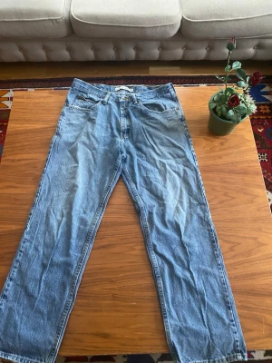 Blå Lee jeans 36/30 straight fit - Klassiska blå Lee jeans i rak modell med fem fickor och snyggt Lee-läderpatch bak. Jeansen är tillverkade i 100% bomull och har en tidlös look som passar till det mesta. Perfekta för dig som gillar en enkel och clean stil.