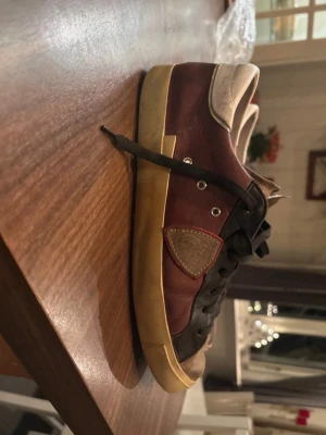 Philippe Model  - Säljer ett par Philippe Model sneakers i vinröd färg med svarta detaljer och vit häl. Klassisk låg modell med svart snörning, beige sula och rund tå. Märkets logga på sidan och bak på hälen. Perfekta för dig som gillar stilrena men unika sneakers. Riktigt bra skick och skorna är i riktigt bra skick till ett bra pris. Box skickas med vid snabb och smidig affär 