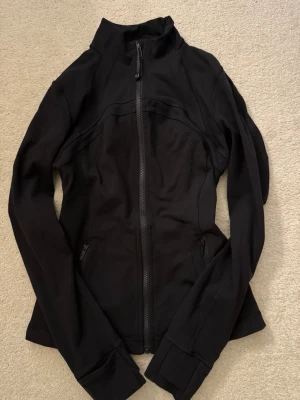 Lululemon Define Jacket - Säljer en svart, figurnära träningsjacka från Lululemon med hög krage och hel dragkedja framtill. Jackan har långa ärmar med tumhål och diskret logga på ryggen. Den är i bra skick då den ej är använd så mycket.                    Nypris: 1300kr