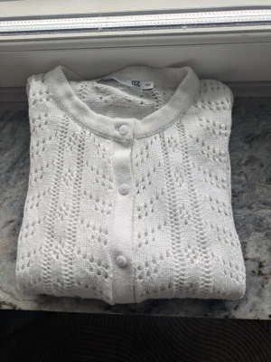 Vit stickad kofta med hålmönster - Supersöt vit stickad kofta med hålmönster och rund hals. Koftan har knappar framtill och är långärmad. Perfekt för lager på lager och ger en fräsch look till alla outfits. Passar dig som gillar klassisk och clean stil. Storlek 150 men passar mig som är xs vanliga fall. Tröjan har några små fläckar men inte vad jag tycker syns, nypris 120
