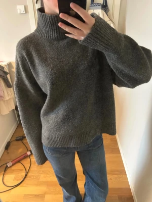 Grå polotröja från Zara - Mysig grå polotröja från Zara i storlek L. Skulle säga att den är som en M. Tröjan har en hög, ribbad krage och långa ärmar med ribbade muddar. Materialet är stickat och känns riktigt skönt mot huden. Passformen är loose och perfekt för chill dagar.