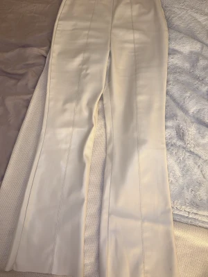 Beige / vita byxor i skinnimitation - Säljer ett par snygga beige byxor i skinnimitation med avsmalnande passform och markerade sömmar längs framsidan. Byxorna har hög midja och ger en clean look. Passar till Petite i längd.