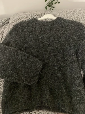 Mörkgrå fluffig stickad tröja Gina Tricot - Mysig mörkgrå stickad tröja från Gina Tricot i fluffigt material. Tröjan har rund halsringning och långa ärmar, perfekt för kyliga dagar. Enkel att styla med jeans eller kjol för en avslappnad look.