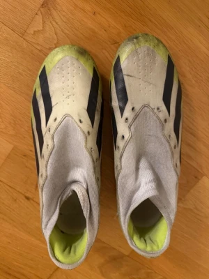 Adidas Crazyfast fotbollsskor vit/gul PRO  - Säljer ett par Adidas Crazyfast fotbollsskor i vitt och neongult med svarta ränder. Skorna har strumpliknande skaft och mönstrad sula för bra grepp på planen. Tillverkade i syntetmaterial och designade för fart och kontroll.