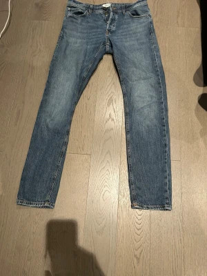 Jeans Jack and Jones  - Säljer ett par klassiska blå jeans i modellen Tapered/Mike. Jeansen har en snygg tvätt, raka ben med avsmalnande passform och fem fickor. Perfekta för dig som gillar en enkel men stilren look. Materialet är slitstarkt jeans och färgen är mellanblå. Storlek 30/34  Hör av er för fler frågor😊