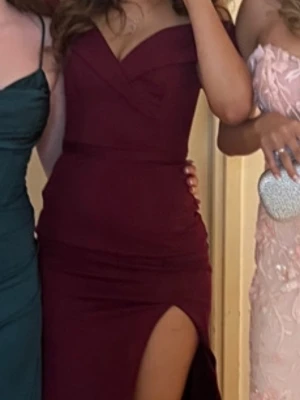 Vinröd balklänning med slits - Säljer en vinröd balklänning med figurnära passform och hög slits på ena sidan. Klänningen är axelbandslös/off-shoulder och har en enkel, elegant design utan mönster. Perfekt för bal eller festliga tillfällen.