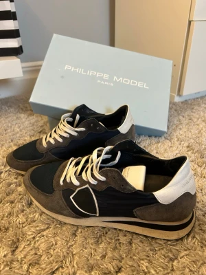 Philippe Model skor - Snygga Philippe Model sneakers i mörkblått och grått med vita detaljer. Ovandelen är i mocka och skinn, med vita skosnören.