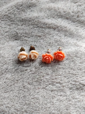 Rosformade örhängen i två färger - Två par söta örhängen i form av rosor, ett par i ljusbeige och ett par i korallorange. Örhängena är små och har metallstift. Perfekta för dig som gillar blommiga detaljer och vill addera något gulligt till din stil.
