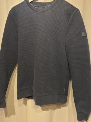 Mörkblå strukturerad sweatshirt Cavallaro Napoli - Säljer en mörkblå sweatshirt med strukturerat tyg och rund hals. Tröjan har ribbade muddar vid ärmslut och nederkant samt en diskret patch på ena ärmen. Perfekt för en avslappnad och stilren look.