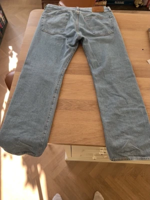 Ljusblå 501 Levi's jeans - Säljer ett par klassiska ljusblå jeans från Levi's med rak passform och fem fickor. Jeansen har en vintage vibe och är tillverkade i 100% bomull. Perfekta för en avslappnad och tidlös stil.