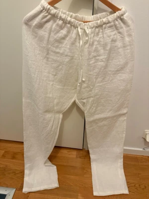 Vita linnebyxor från Lin Living - Snygga och luftiga vita linnebyxor från Lin Living i 100% ekologiskt odlat lin. Byxorna har resår och dragsko i midjan för skön passform. Perfekta för en avslappnad och stilren look.