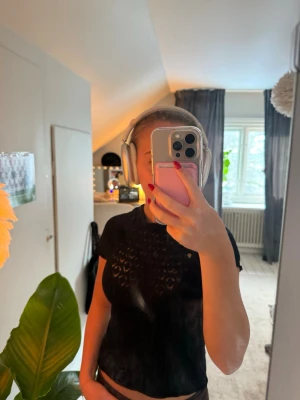 Svart topp med spetsdetaljer - Snygg svart topp med korta ärmar och genombrutna spetsdetaljer upptill. Toppen har en figurnära passform och är perfekt för att lyfta en outfit med lite extra edge. Materialet ser ut att vara spets