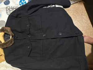 Svart overshirt med fuskpälsdetalj - Stilren svart overshirt med två stora bröstfickor och knappar framtill. Kragen har en snygg fuskpälsdetalj som ger extra edge. Perfekt lager på lager-plagg för dig som gillar en clean look. Materialet känns tjockt och värmande.