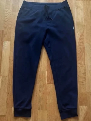 Polo Ralph Lauren Byxor - Snygga marinblå mjukisbyxor från Polo Ralph Lauren med broderad vit logga på höften. Tillverkade i mjukt, dubbelt stickat material för extra komfort. Inga skador eller hål, men kan vara lite noppriga på grund av användning – därav priset. Nypris ca 2000 kr. 