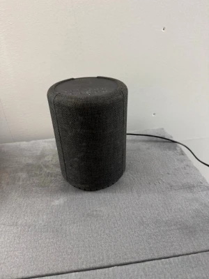 Audio Pro svart bärbar högtalare - Snygg svart bärbar högtalare från Audio Pro med rundad cylinderform och tygklädd yta. Smidiga knappar på ovansidan för volym och uppspelning samt anslutning via WiFi och AUX. Perfekt för att streama musik.