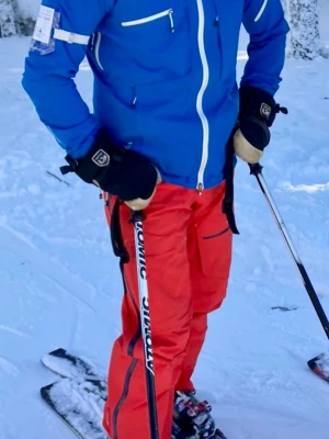 Peak Performance -blå skidjacka och röda skidbyxor med hängslen - Säljer en blå skidjacka och ett par röda skidbyxor från Peak Performance med svarta hängslen och dragkedjeförsedda fickor. Byxorna är tillverkade i slitstarkt material, perfekta för skidåkning och vinteraktiviteter. Snygg passform och praktiska detaljer för aktiva dagar i backen. Litet hål i ena byxbenet och fläckar i grenen (går troligtvis att tvätta bort.)