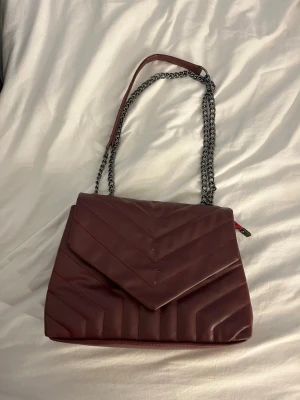 Vinröd quiltad axelväska med kedja - Snygg vinröd axelväska . Aldrig använd men köpt utomlands och har skadats lite under resan hem !!