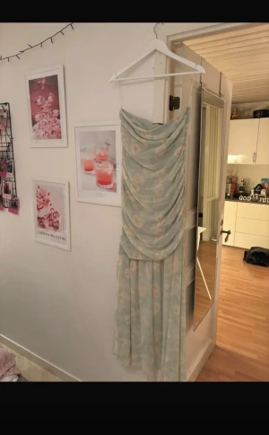 Ljusgrön blommig långklänning Adoore - Superfin ljusgrön långklänning från Adoore med blommigt mönster och draperad framsida. Klänningen har tunna axelband och en romantisk, flowy siluett. Perfekt för sommarens alla tillfällen.