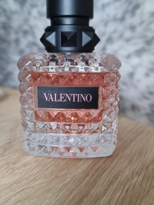 Valentino Donna Born In Roma parfym - Valentino Donna Born In Roma är en lyxig parfym i en snygg, rosa och transparent glasflaska med nitar på korken. Flaskan rymmer 50 ml och har en exklusiv design med mönstrad yta och svart etikett. Perfekt för dig som gillar eleganta och trendiga dofter. Endast testad nyligen.