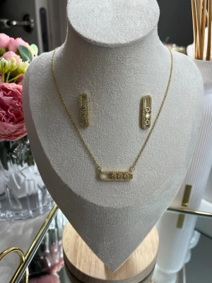 18k guldpläterat Messika set - Smyckesetet innehåller ett halsband och örhängen i 18k guldpläterat rostfritt stål, dekorerade med fina strassdetaljer