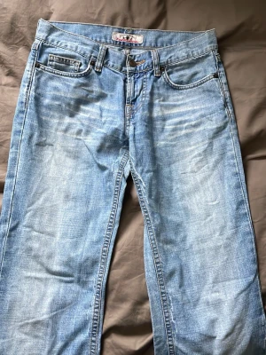 Vintage ljusblå jeans från Fornarina - Säljer ett par klassiska ljusblå jeans från Fornarina med fem fickor och snygga slitningar framtill. Jeansen har raka ben med lite bootcut och detaljerade bakfickor med broderi. Lågmidjade i storlek 28. 