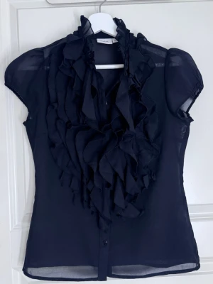 Svart volangblus från Saint Tropez - Säljer en superfin svart blus från Saint Tropez med volangdetaljer framtill och lätt transparent tyg. Väldigt elegant och perfekt till fest, middag eller en mer uppklädd look❤️Storlek XS, knappt använd