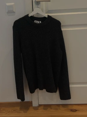 Svart/Grå stickad tröja från Weekday - Mysig svart stickad tröja från Weekday med rund halsringning och långa ärmar. Tröjan har en enkel och stilren design, perfekt för lager på lager och passar till det mesta. En stickad tröja, perfekt nu när det är kallare ut!