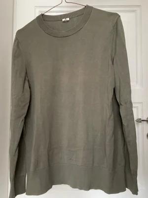 Stickad Tröja Arket - Enkel och stilren olivgrön tröja med rund halsringning och långa ärmar. Tillverkad i mjuk bomull med ribbade muddar vid hals, ärmslut och nederkant. Perfekt för en clean och avslappnad look.