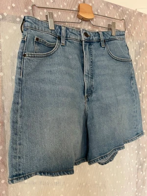 Blå högmidjade jeansshorts - Klassiska blå jeansshorts med hög midja och fem fickor. De har en avslappnad passform och stängs med knapp och dragkedja. Perfekta för varma dagar och enkla att matcha med olika toppar.