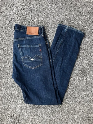 Blå jeans från replay - Mörkblå jeans från replay med klassisk femficksmodell och raka ben. Snygga kontrastsömmar och detaljerad bakficka med broderad design. Tillverkade i slitstark denim med läderpatch bak i midjan. Perfekta för en avslappnad och stilren look.