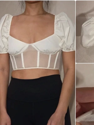 Vit croppad topp från Zara - Trendig vit croppad topp från Zara med puffärmar och fyrkantig urringning. Toppen har meshdetaljer och markerade sömmar framtill som ger en snygg corset-look. Perfekt för att lyfta din outfit med en modern touch.