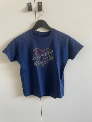 Blå t-shirt med hjärtmotiv Zadig & Voltaire - Blå t-shirt från Zadig & Voltaire med ett stort hjärtmotiv i glittriga färger på bröstet. Klassisk rund hals och korta ärmar. Perfekt för dig som vill ha en cool och färgglad detalj i garderoben.