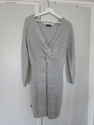 Grå stickad klänning strl L passar M - Storlek L men sitter bra på M. Mysigt grå stickad klänning från Tally Weijl med twistad detalj framtill och v-ringad hals. Klänningen har trekvartsärm och är i mjukt stickat material, perfekt för kyligare dagar. Snygg och enkel att styla med boots eller sneakers.