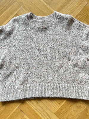 Beige melerad stickad tröja strl M  - Mysig beige stickad tröja med melerat mönster i brunt, rosa och grått. 4% ull. Tröjan har rund halsringning och ribbstickade muddar vid hals, ärmslut och nederkant. 