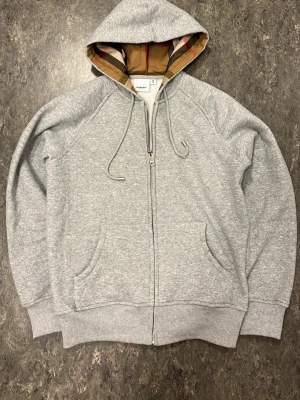 Grå hoodie från Burberry med dragkedja - Nyskick. Knappt använd. Tröjas är i storlek M men sitter mer som S.