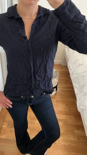 Mörkblå klassisk skjorta - Säljer en mörkblå skjorta med klassisk krage och knappar framtill. Skjortan har lång ärm och en enkel, tidlös design som passar till det mesta. Materialet känns lätt och mjukt mot huden.