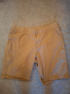 Beiga cargoshorts med fickor - Snygga beiga cargoshorts med flera praktiska fickor framtill och på sidorna. Klassisk passform med bälteshällor och knappstängning. Perfekta för sommardagar och avslappnade outfits.