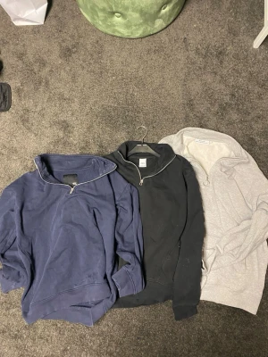 3 halvzip-tröjor i blått, svart och grått - Tre stilrena halvzip-tröjor i blå, svart och ljusgrå färg. Alla har hög krage med dragkedja och är tillverkade i mjukt sweatshirtmaterial. Perfekta för en avslappnad och trendig look. Säljes tillsammans.   Den blåa o svarta tror jag är i S o den gråa är i L eller xl 