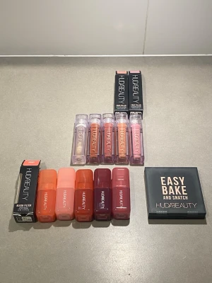 Huda Beauty Smink Kollektion Värde ca 3500kr  - Hudabeauty smink kollektion innehållande Faux filler lip gloss i 5 populära färger, liquid blush filter också i 5 populära färger och Easy Bake and Snatch Pressed Powder.   Blush: Peach Sorbet, Cotton Candy, Strawberry  Cream, Watermelon Pop, Black Cherry.  Läppglans: Glassy, Foxy, Honey, Bombshell, Sugar Baby.  Puder: Easy Bake and Snatch i nyansen Pound Cake.  Det mesta är testat 1 gång bara Peach sorbet blush oanvänd.