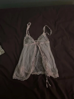 Ljusrosa spetsbody med rosett - Söt ljusrosa body i transparent mesh med prickigt mönster och spetsdetaljer. Justerbara axelband och dekorativ rosett framtill. Materialet är tunt och luftigt, perfekt för dig som gillar romantisk stil på underkläder. Heta upp kvällen 🫶🏼 