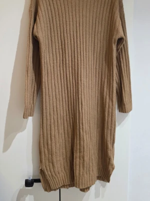 Beige ribbstickad lång tröja - Säljer en beige ribbstickad lång tröja med långa ärmar. Tröjan har en rak passform och är tillverkad i ett mjukt, tjockare stickat material som ger en mysig känsla. Perfekt för lager på lager och enkel att styla till olika outfits.