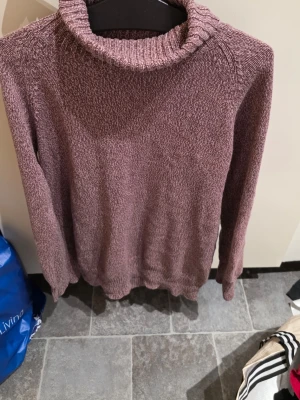 Stickad polotröja i lila melange - Mysig stickad polotröja i lila melange med lång ärm och ribbad krage. Tröjan har en avslappnad passform och är tillverkad i ett mjukt garn som känns skönt mot huden. Perfekt för kyliga dagar och enkel att matcha med jeans eller kjol.